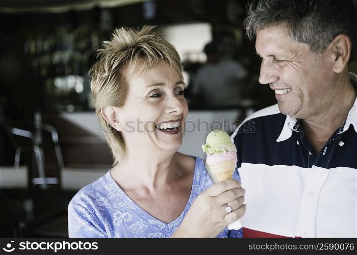 Mature woman holding an ice-cream cone with a senior man smiling beside her