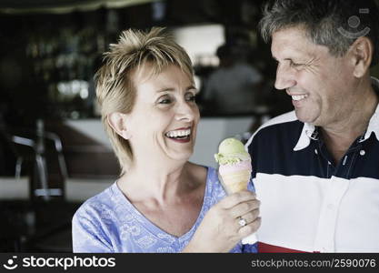 Mature woman holding an ice-cream cone with a senior man smiling beside her