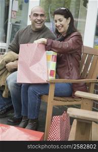Mature woman holding shopping bags and smiling with a mid adult man sitting beside her