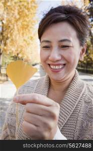 Mature Woman Holding Yellow Ginkgo Leaf