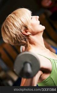 Mature woman in a gym exercising by lifting a barbell