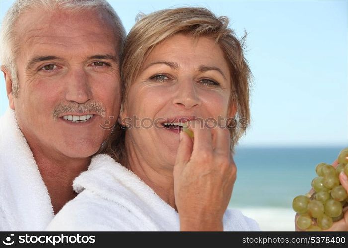 mature woman in bathrobe at spa resort eating grapes with husband
