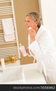 Mature woman in bathroom clean face make-up removal looking mirror