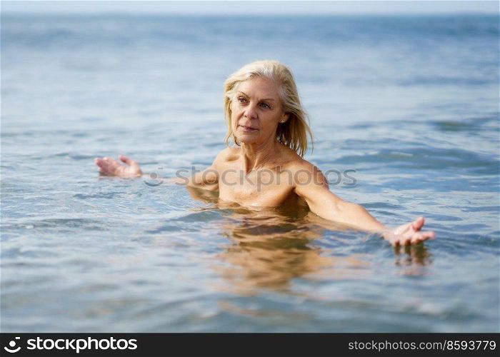 Mature woman in good shape bathing in the sea. Elderly female enjoying her retirement at a seaside retreat.. Eldery woman in good shape bathing in the sea.
