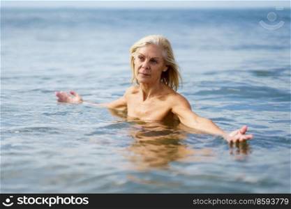 Mature woman in good shape bathing in the sea. Elderly female enjoying her retirement at a seaside retreat.. Eldery woman in good shape bathing in the sea.