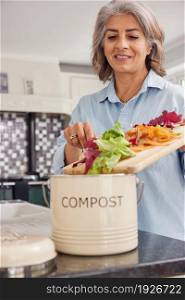 Mature Woman In Kitchen Making Compost Scraping Vegetable Leftovers Into Bin