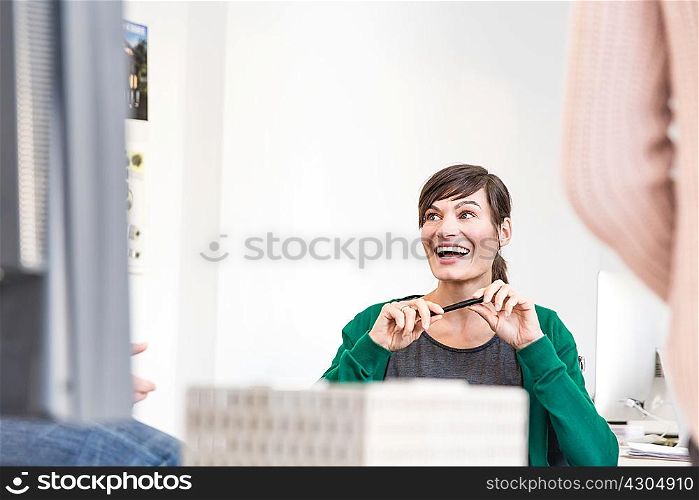 Mature woman in office talking to colleagues holding pen looking away smiling