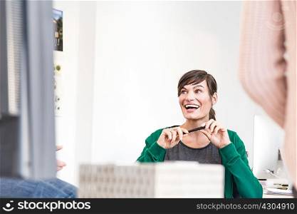 Mature woman in office talking to colleagues holding pen looking away smiling