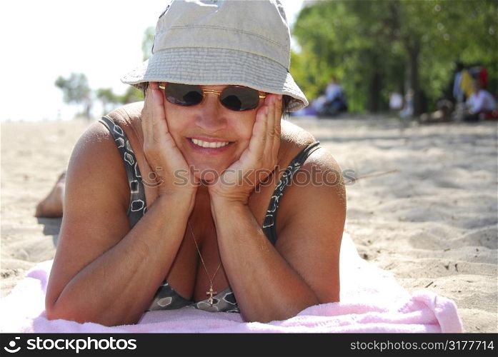 Mature woman in sunglasses lying on a sandy beach