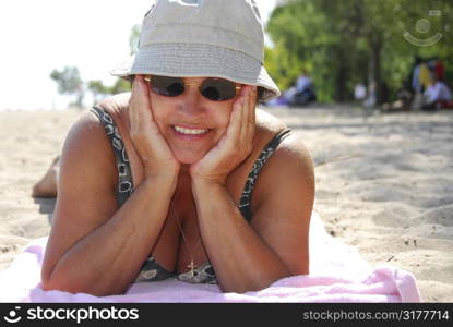 Mature woman in sunglasses lying on a sandy beach