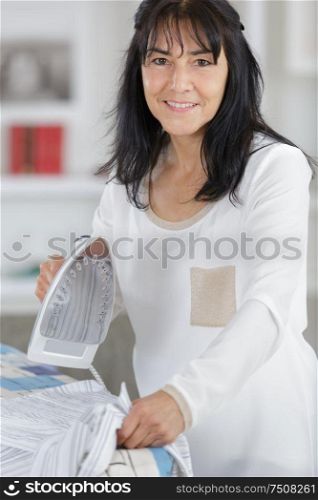 mature woman ironing clothes in her home