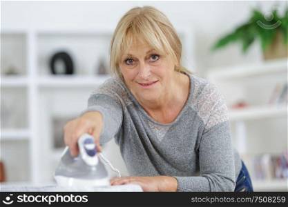 mature woman ironing clothes on an ironing board