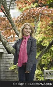 Mature woman leaning against a maple tree and smiling