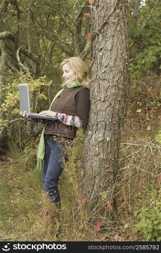 Mature woman leaning against a tree and using a laptop