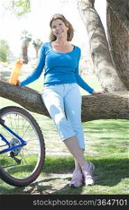 Mature woman leans on tree with her bike