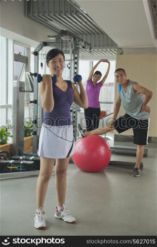 mature woman lifting weights in the foreground, people exercising in the background