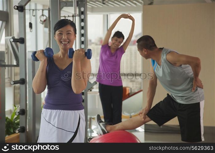 mature woman lifting weights in the foreground, people exercising in the background