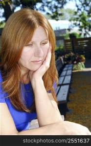 Mature woman looking sad and depressed sitting alone on a park bench