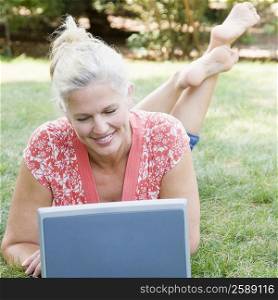 Mature woman lying in a park and using a laptop