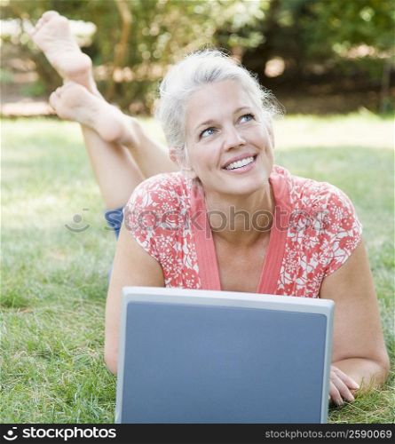 Mature woman lying in a park in front of a laptop and smiling