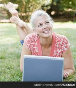 Mature woman lying in a park in front of a laptop and smiling