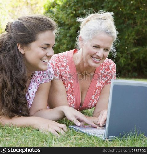 Mature woman lying in a park with her daughter and using a laptop