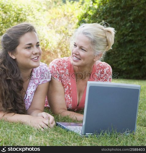 Mature woman lying in a park with her daughter and using a laptop