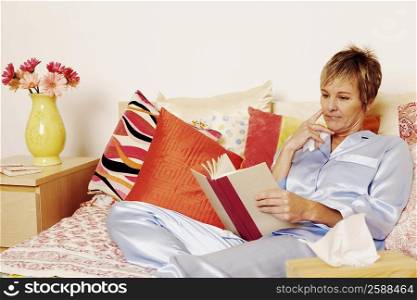 Mature woman lying in bed and reading a book