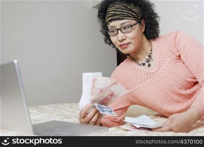 Mature woman lying in front of a laptop holding paper currency