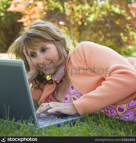 Mature woman lying on grass and using a laptop