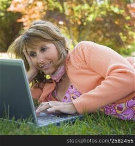Mature woman lying on grass and using a laptop