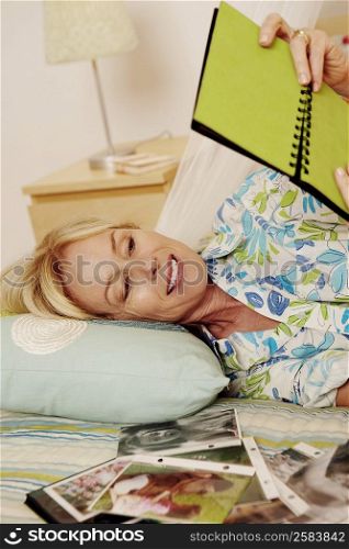 Mature woman lying on the bed and looking a photo album