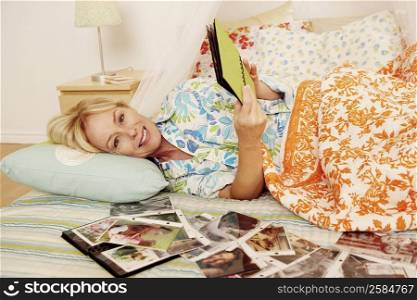 Mature woman lying on the bed and looking a photo album