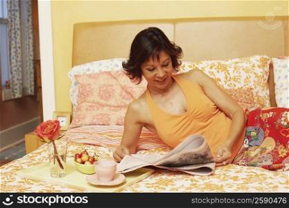 Mature woman lying on the bed and reading a newspaper