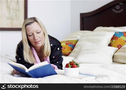 Mature woman lying on the bed reading a book