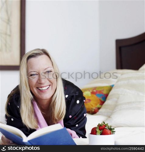 Mature woman lying on the bed with a book and smiling