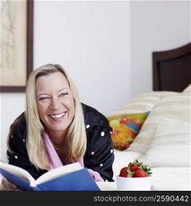 Mature woman lying on the bed with a book and smiling