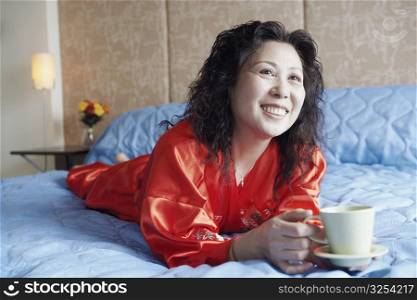 Mature woman lying on the bed with a cup of tea smiling
