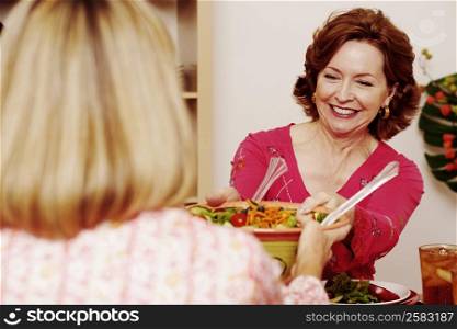 Mature woman passing a bowl of salad to her friend and smiling