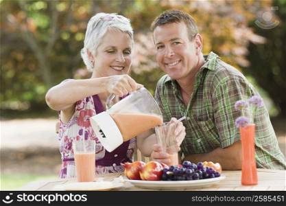 Mature woman pouring juice in a glass with a mature man smiling beside her