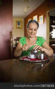 Mature woman pouring sugar into a cup of tea