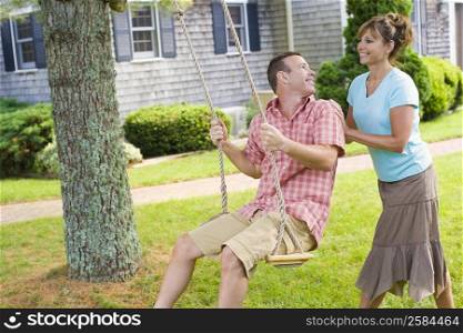 Mature woman pushing a mature man on a rope swing and smiling