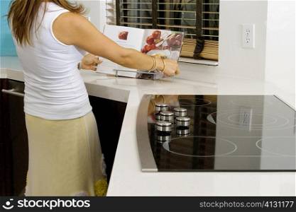 Mature woman reading a cookbook at a kitchen counter