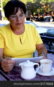 Mature woman reading papers in outdoor cafe looking concerned