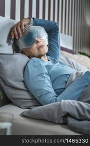 Mature woman relaxing at home, wearing cooling blue gel eye mask against dark circles.. Mature Woman Wearing Cooling Blue Gel Eye Mask Against Dark Circles