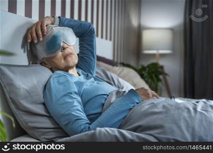 Mature woman relaxing at home, wearing cooling blue gel eye mask against dark circles.. Mature Woman Wearing Cooling Blue Gel Eye Mask Against Dark Circles