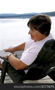 Mature woman relaxing on a pier in a wooden chair