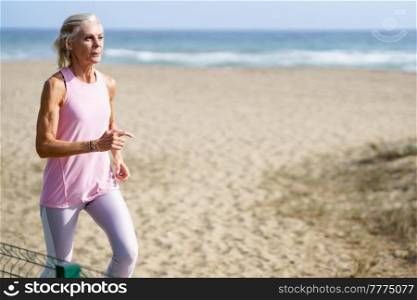 Mature woman running along the shore of the beach. Older female doing sport to keep fit. Concept of healthy living in the elderly. Senior woman in fitness clothing running along beach. Mature woman running along the shore of the beach. Older female doing sport to keep fit