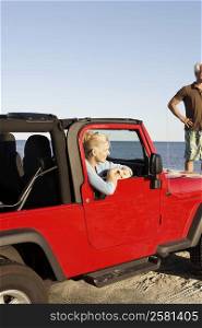 Mature woman sitting in a sports utility vehicle with a mature man standing with arms akimbo