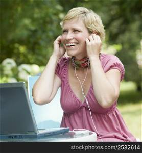Mature woman sitting in front of a laptop and listening to an mp3 player
